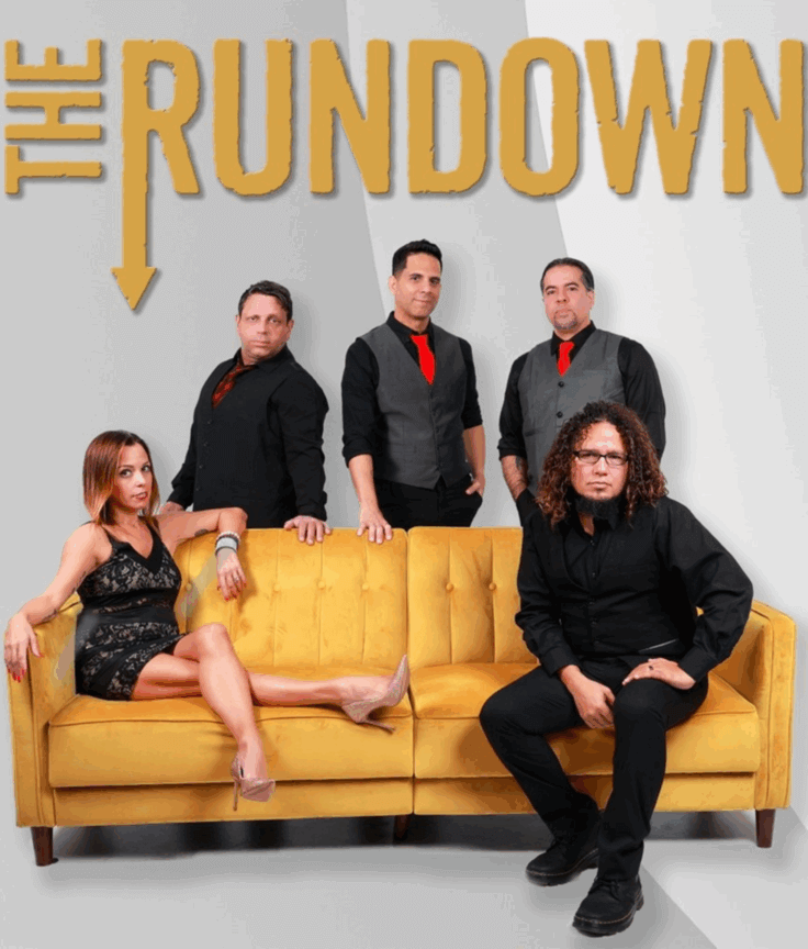 Five people pose on and behind a yellow couch under the words The Rundown. Four men stand or sit, dressed in black with red ties, while a woman in a sparkly dress lounges on the couch. The background is white and gray.